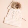 Cream Cable Knit Bobble Hat on a Beige Background