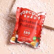 Popcorn Shed Christmas Pudding Popcorn Snack Pack in a small red packet on a beige background with a snowy backdrop