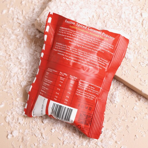 Back of Packaging Back of Popcorn Shed Christmas Pudding Popcorn Snack Pack in a small red packet on a beige background with a snowy backdrop