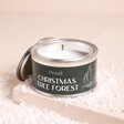 A Small Metal Tin Candle With a Green Festive Label Sitting on a Neutral Background