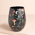 A Black Matte Effect Stemless Wine Tumble With a Woodland Themed Pattern on a Neutral Surface