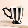 A mug with vertical black and white chunky stripes and a batwing shaped handle.