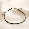 A black rope corded bracelet with gold beads woven round the outside circumference finished with a pull cord closure