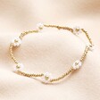 Stainless Steel White Daisy Beaded Bracelet in Gold on a Beige Background.