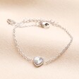 This charmig bracelet features a small, dainty, textured heart charm on top of a trace chain with an extender.