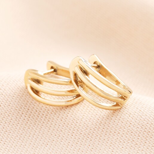 Stainless Steel Illusion Huggie Hoop Earrings in Gold on a Beige Background. A pair of huggie earrings with a triple earring illusion that connects at the earring hole.