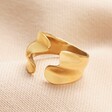 Stainless Steel Open Wave Adjustable Ring in Gold on a Beige Background.