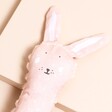 Close up of light pink Trixie Bunny Baby Squeaker Toy with floppy ears on a beige background