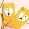 Yellow Trixie lion socks with a smiling face and white dot details. Two pairs shown on a beige background.