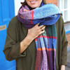 A Model Wearing a Tartan Check Print Knitted Scarf in Bright Colours With a Khaki Green Coat