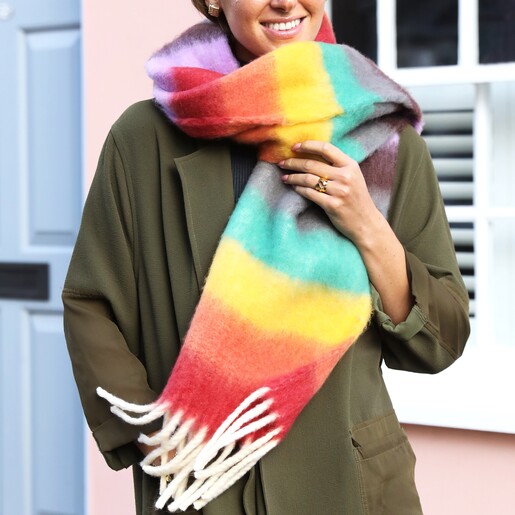 Rainbow Thick Stripe Winter Scarf A Model Wearing a Green Coat and a Chunky Blanket Scarf in a Bright Rainbow Stripe Print