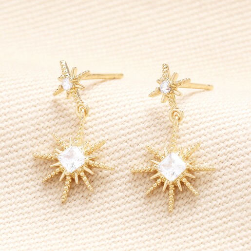 Close up of Crystal Double Star Drop Earrings in Gold on a neutral background