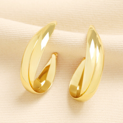 Gold organic interlocking hoop earrings displayed on cream fabric
