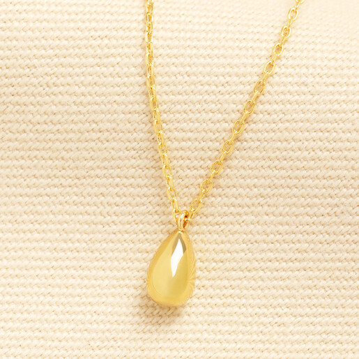 Gold teardrop pendant necklace on a fine trace chain against textured cream fabric