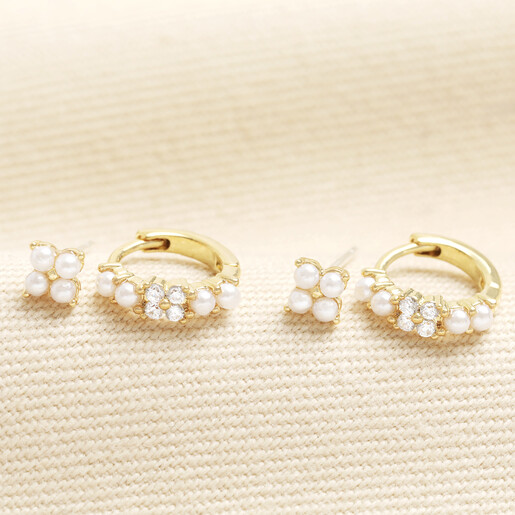 Set of gold pearl stud and huggie hoop earrings on a light textured background