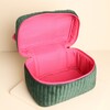 Open green velvet makeup bag revealing the spacious bright pink fabric-lined interior