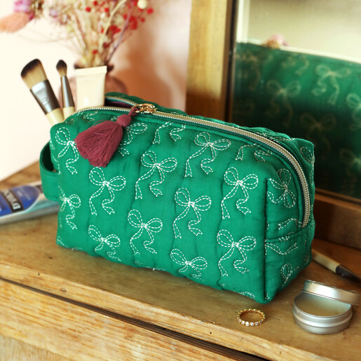 Quilted green makeup bag with embroidered white bows on a wooden vanity