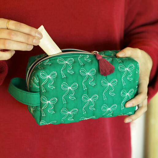 Person holding the green embroidered bow makeup bag and inserting cosmetics