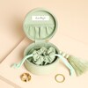 Open green travel jewellery case revealing internal pouch next to two gold rings.