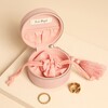 Open pink jewellery case showing drawstring pouch, elastic pocket, and gold rings.