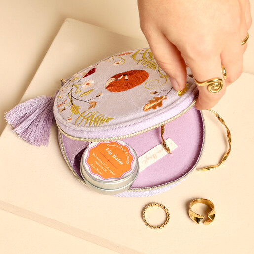 Hand opening purple fox jewellery pouch filled with lip balm and gold rings.