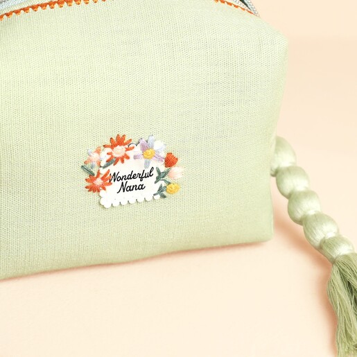 Close-up of embroidered Wonderful Nana floral badge on sage green makeup bag