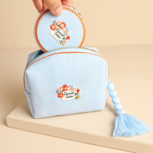 Matching Dearest Sister compact mirror being placed inside the blue embroidered makeup bag
