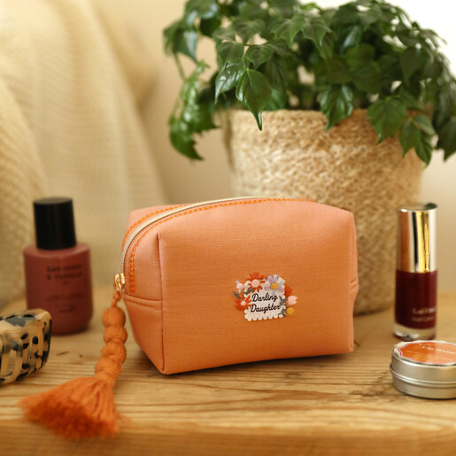 Orange linen Darling Daughter embroidered makeup bag styled on a wooden surface with toiletries