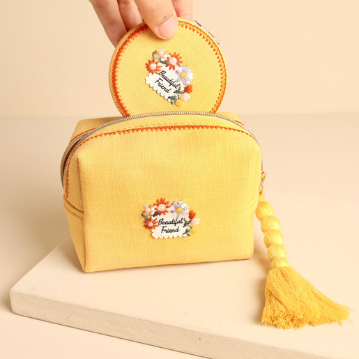 Hand placing matching embroidered compact mirror into yellow Beautiful Friend makeup bag
