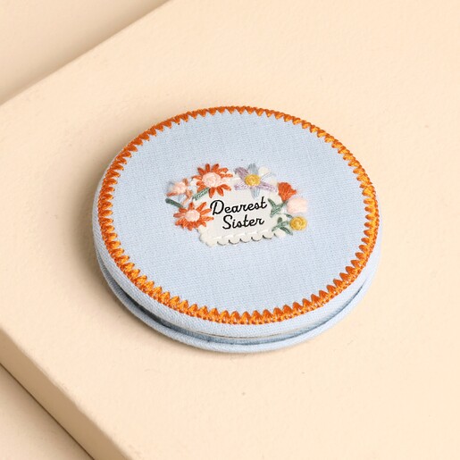 Closed blue fabric pocket mirror with embroidered flowers and Dearest Sister sentiment.