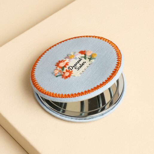 Slightly open blue fabric compact mirror revealing the glass mirror inside.
