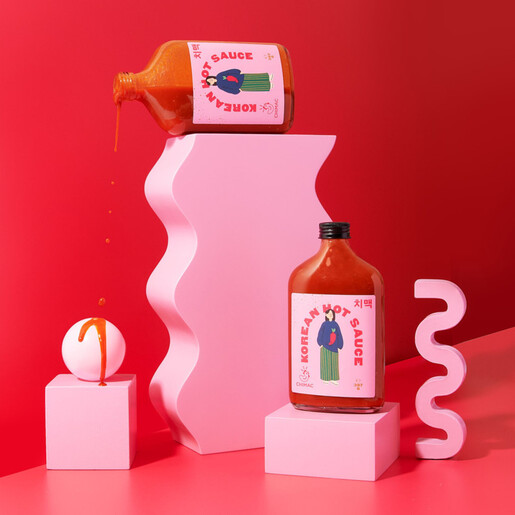 Chimac Korean hot sauce bottles styled on pink display blocks with pouring sauce