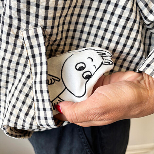 Moomin hand warmer being tucked into a black and white gingham coat pocket.