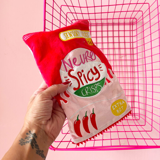 Person holding the Neurospicy crisp packet hot water bottle in front of pink basket