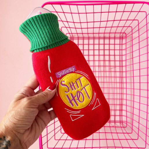 Hand holding the red knitted hot sauce bottle hot water bottle above a pink basket