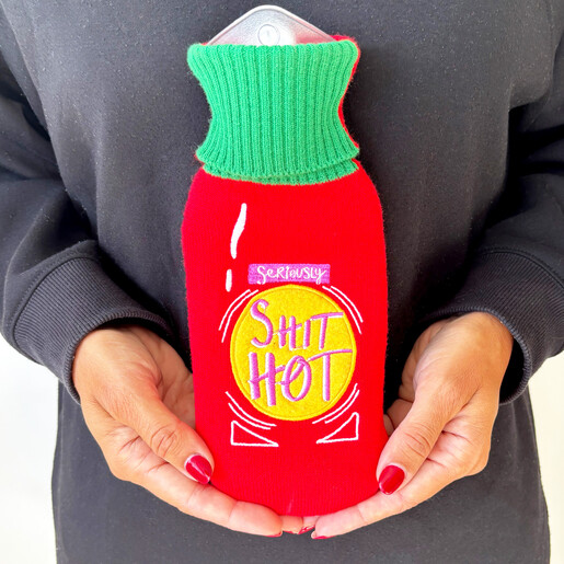 Hands cupping the compact red hot sauce bottle hot water bottle against a dark top