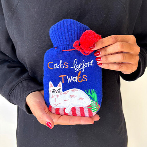 Person holding a blue Cats Before Twats hot water bottle with red pom-poms