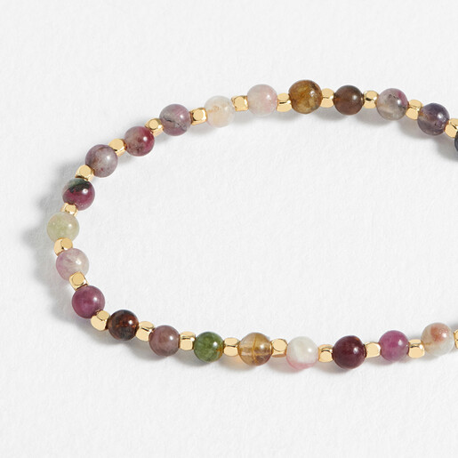 Close up of Estella Bartlett tourmaline and gold beaded bracelet on white surface