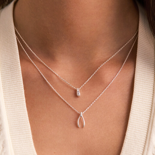 Model wearing the Estella Bartlett delicate silver wishbone pendant necklace layered with another chain