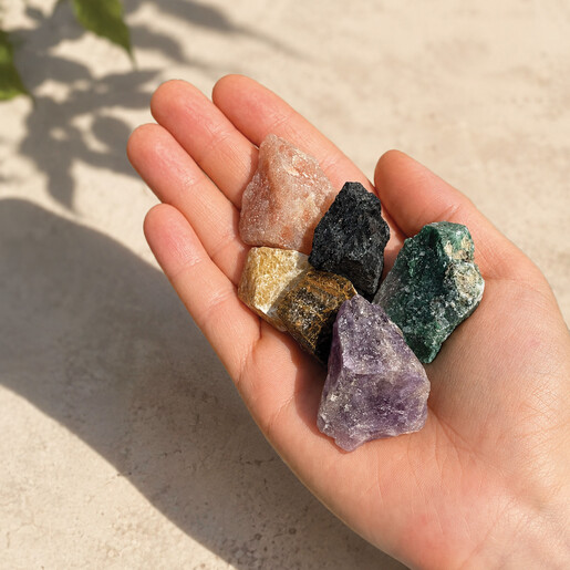 Hand holding six rough, multicoloured crystal stones from the keepsake gift set.