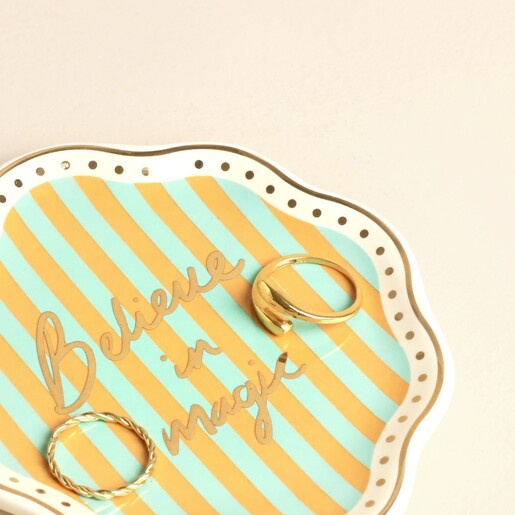 Close up of striped Believe in Magic trinket dish holding two gold rings