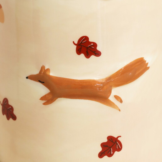 Close-up of the raised orange fox and falling autumn leaves on the mug