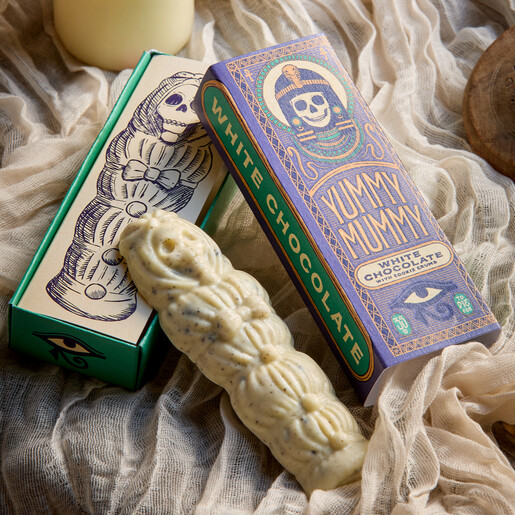 Yummy mummy white chocolate figure resting against an opened sliding illustrated gift box.
