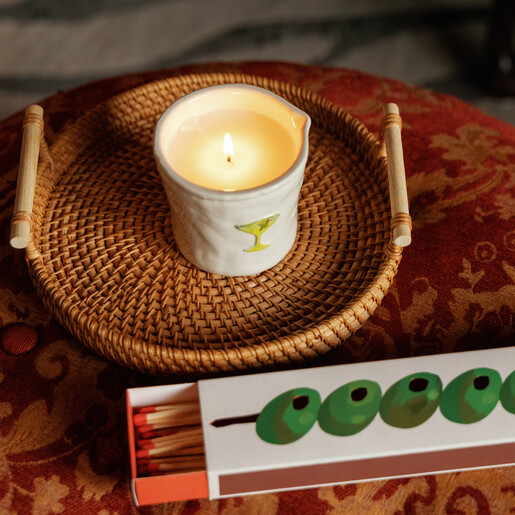 Lit martini candle sitting inside woven wicker tray next to olive matches