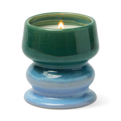 Close-up of lit candle inside glazed green and blue ombre ceramic pedestal vessel