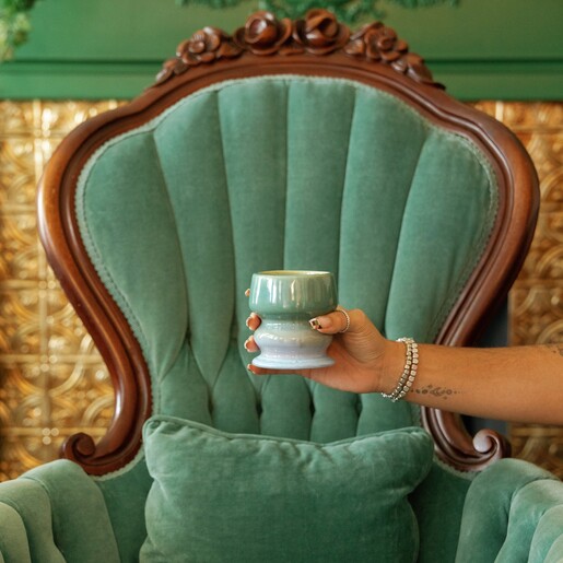Hand holding green and blue ombre ceramic candle in front of a green armchair