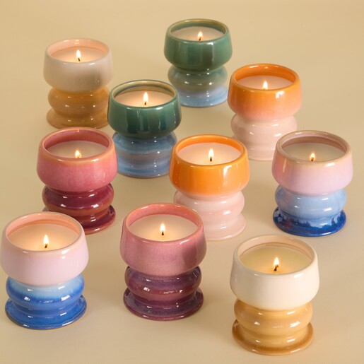 A colourful assortment of lit Paddywax ombre pedestal candles arranged on a table