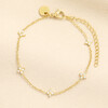 Gold stainless steel chain bracelet with crystal-studded clover charms on cream background