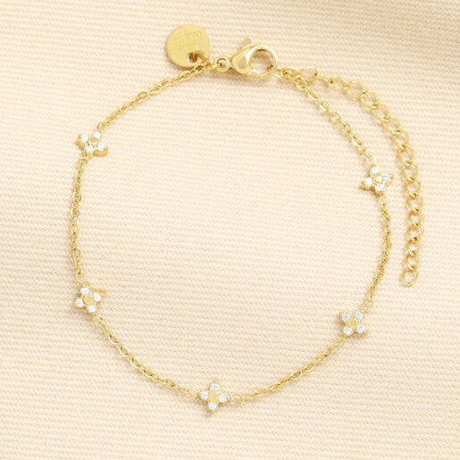 Gold stainless steel chain bracelet with crystal-studded clover charms on cream background