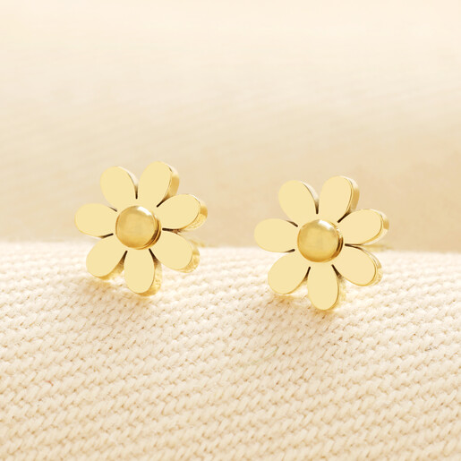 Pair of gold stainless steel daisy stud earrings on textured cream fabric.